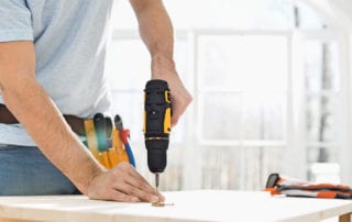 Midsection of man drilling nail on table